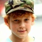 Young boy with freckles and stacked caps in rustic setting