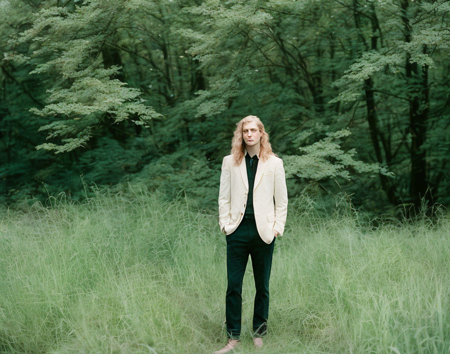 Blonde man in beige jacket standing in green field