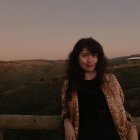 Young woman with black hair in blush jacket standing in dusky landscape