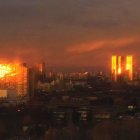 Cityscape painting at dusk: silhouetted buildings, fiery sky, crescent moon