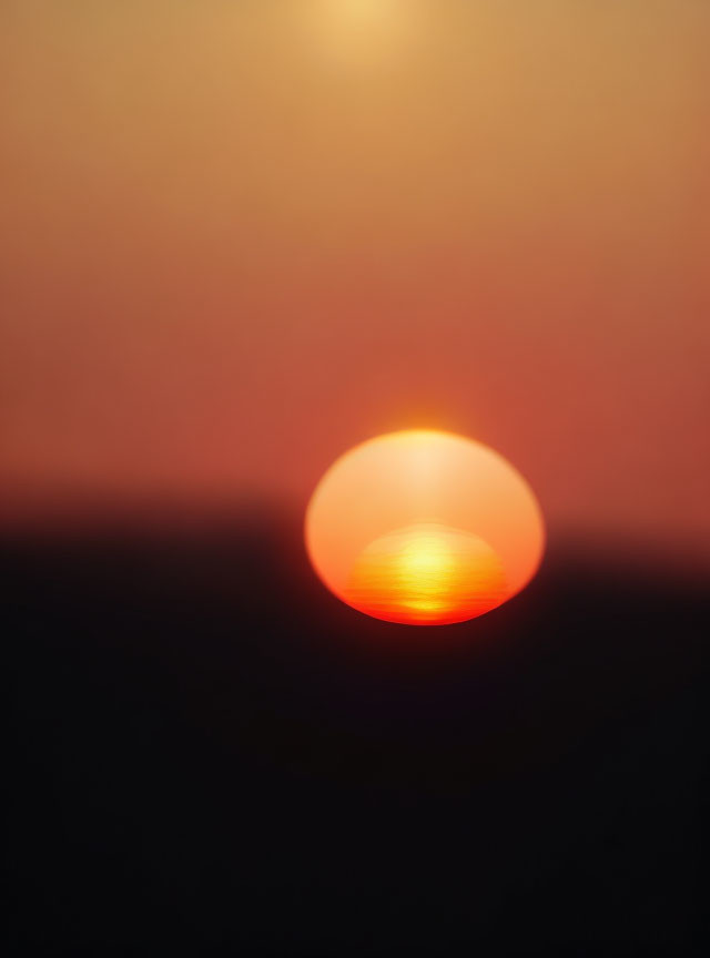 Vibrant red-orange sun setting under hazy sky