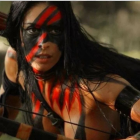 Person in Striking Face Paint & Feathered Headdress Holding Bow