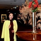 Young Woman in Yellow Coat by Elegant Flower Vase