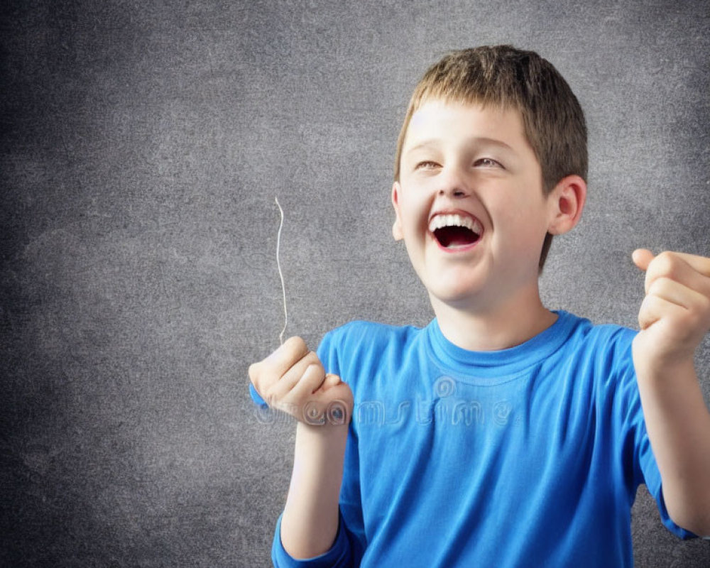 Young boy in blue shirt laughing with textured gray background.