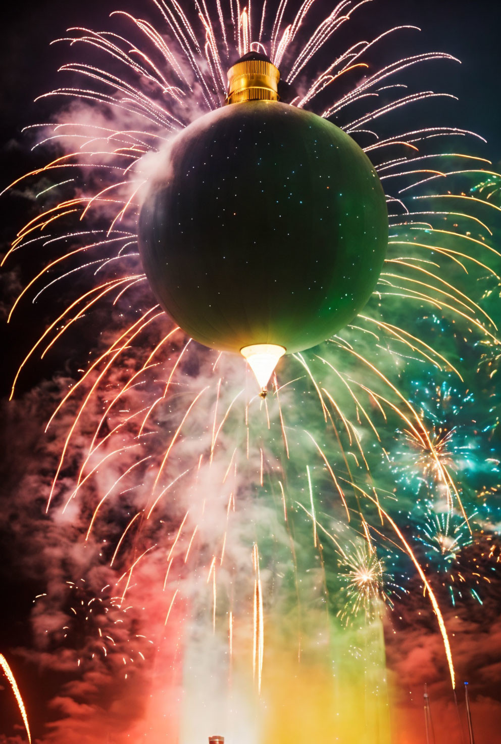 Green Christmas ornament hanging under colorful fireworks on night sky