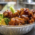 Glazed chicken bowl with broccoli, noodles, dark drink, and green bottle on vibrant background