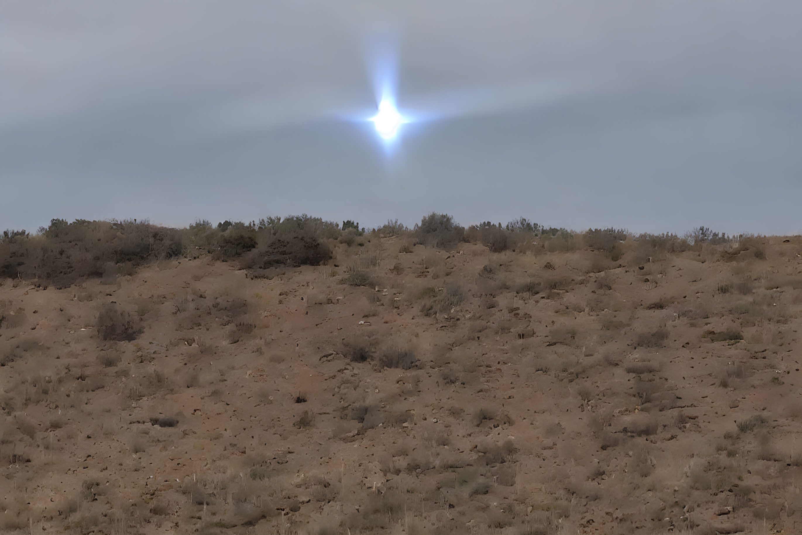 Bright star-like object in cloudy sky over barren, hilly terrain