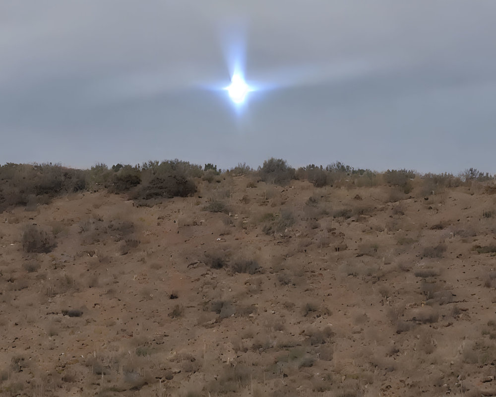 Bright star-like object in cloudy sky over barren, hilly terrain