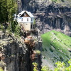 White house on rocky cliff overlooking ocean with lush greenery and white flowers.