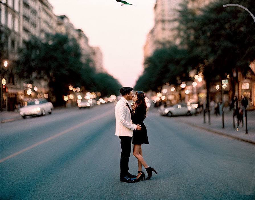 Couple embracing on city street at dusk with blurred background.