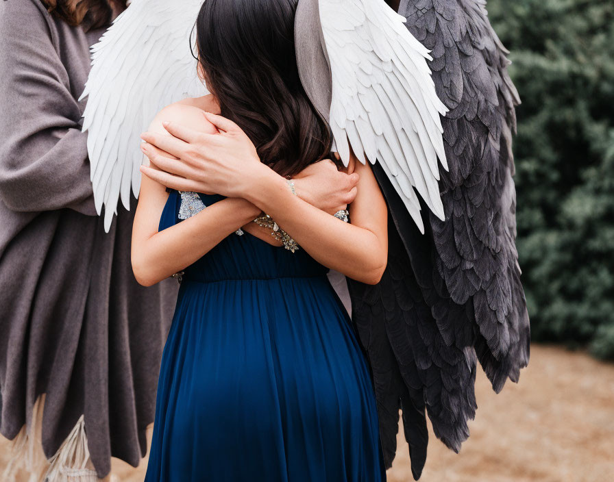 Embrace of two figures with white and black wings in nature.