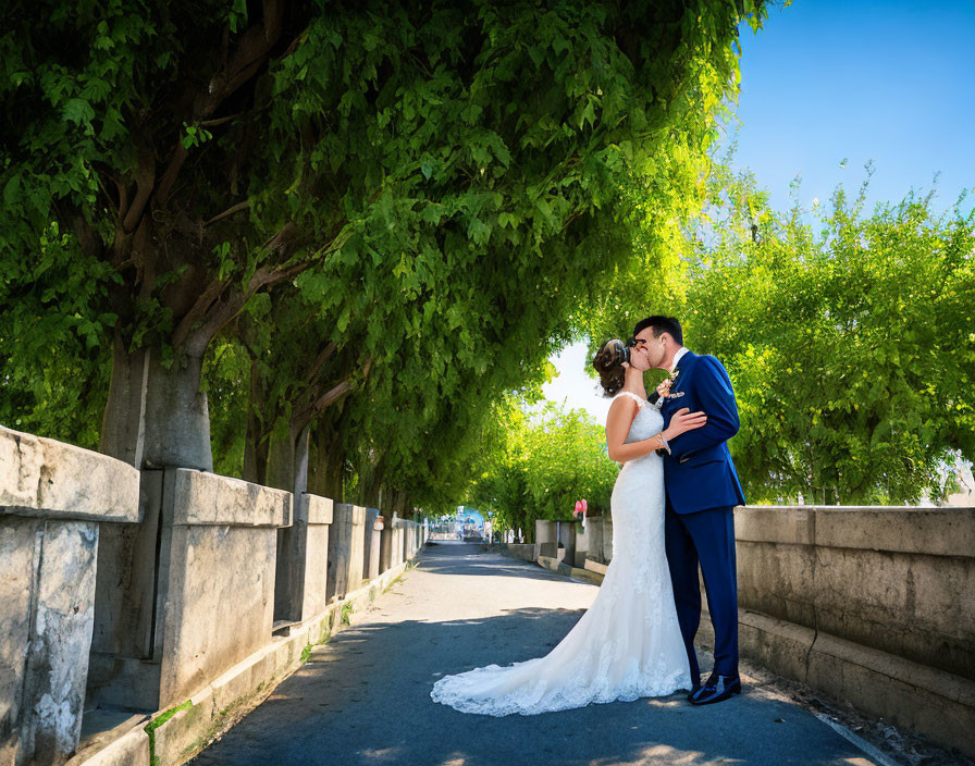 Bride and groom kissing in sunlit path with green trees