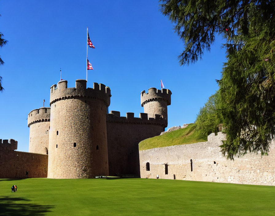 Medieval stone castle with round towers and American flags under clear blue sky