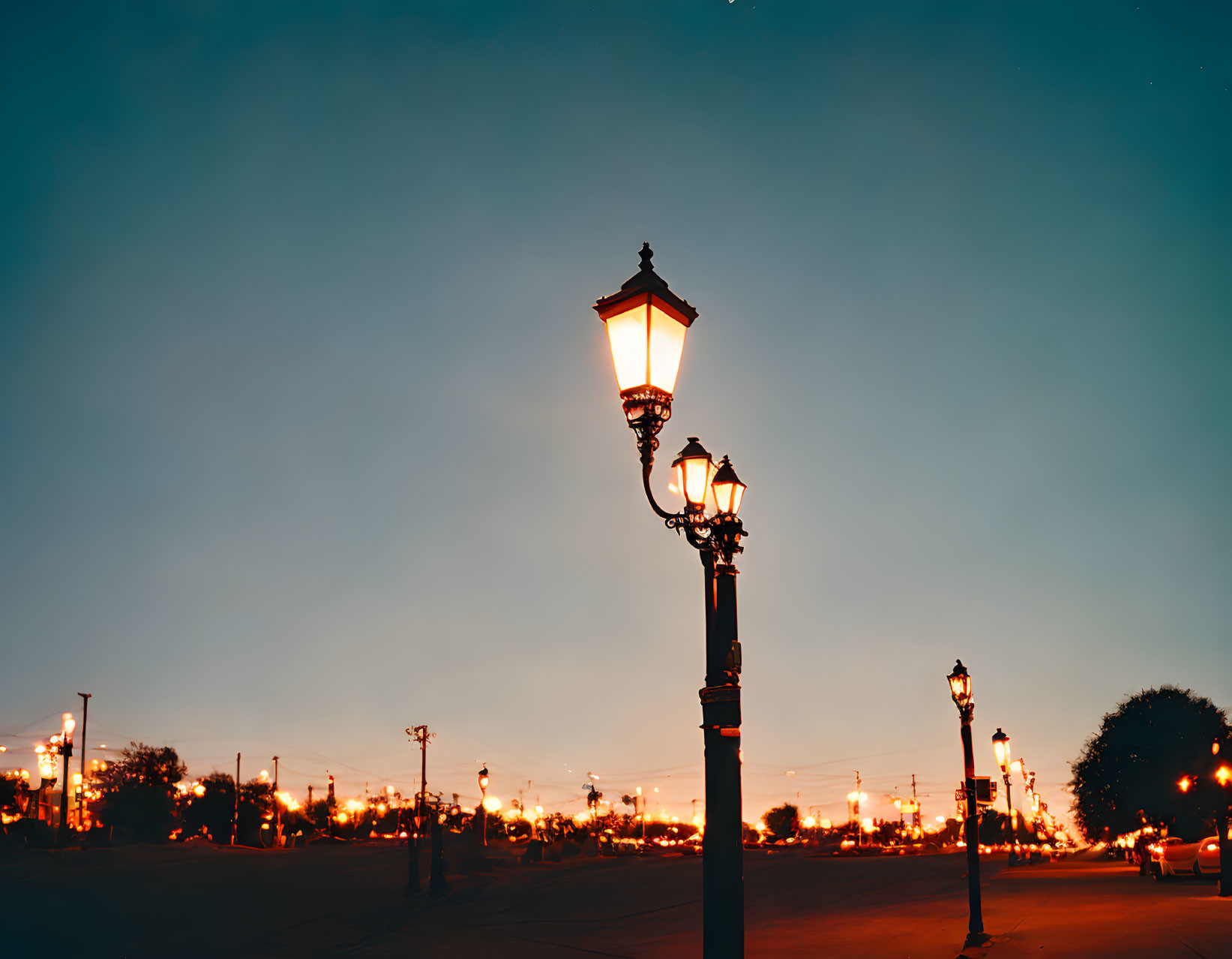 Vintage street lamps illuminated at dusk under blue sky with warm horizon glow.