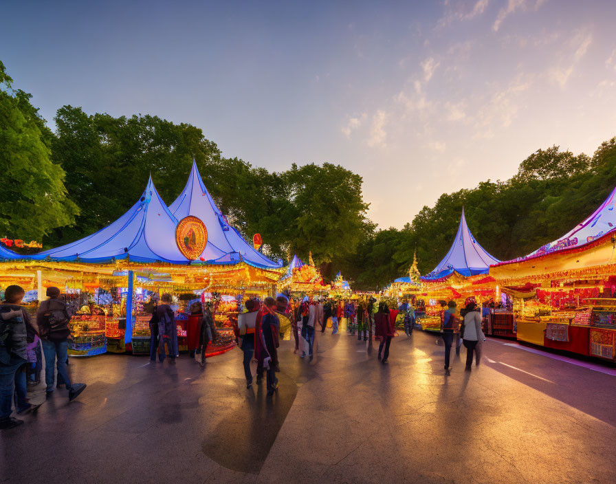 Colorful illuminated stalls at outdoor fair at dusk amid trees