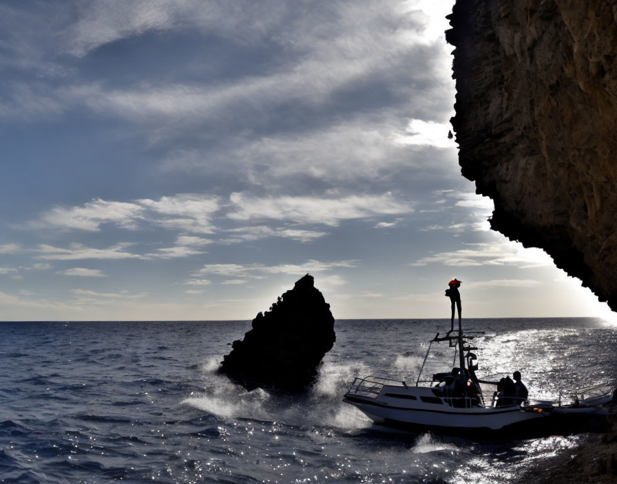 Silhouette of person on boat near rocky outcrop by the sea.