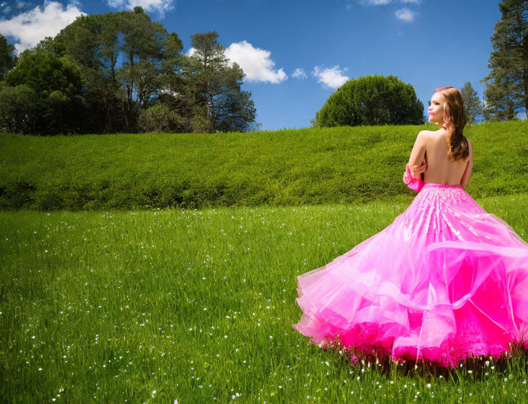 Woman in pink gown in lush green meadow under blue sky