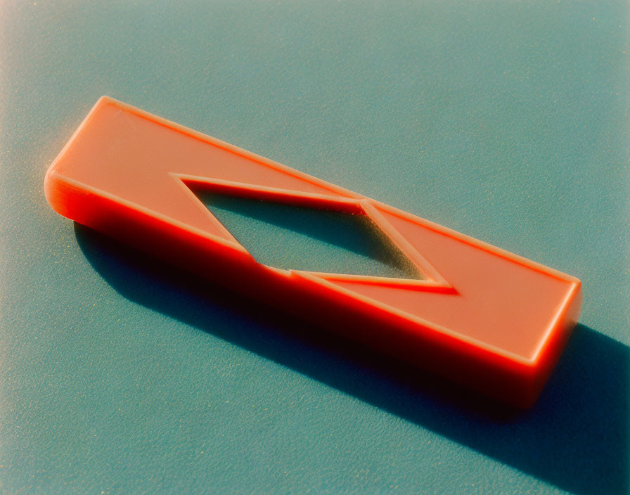 Red plastic kazoo on teal surface with soft shadow