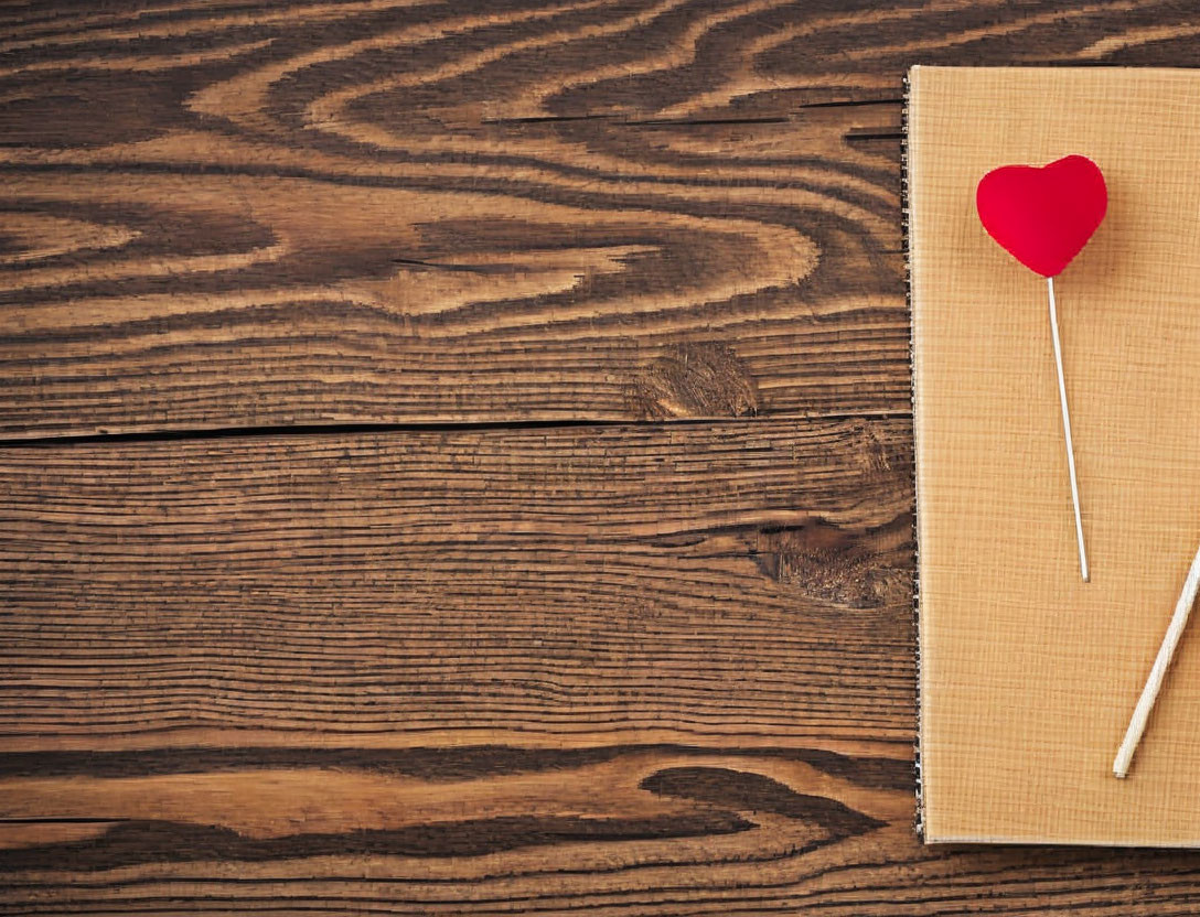 Red heart lollipop on brown notebook on rustic wooden table