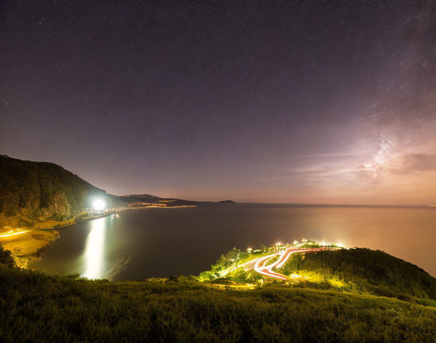 Starry night coastal landscape with illuminated road and town