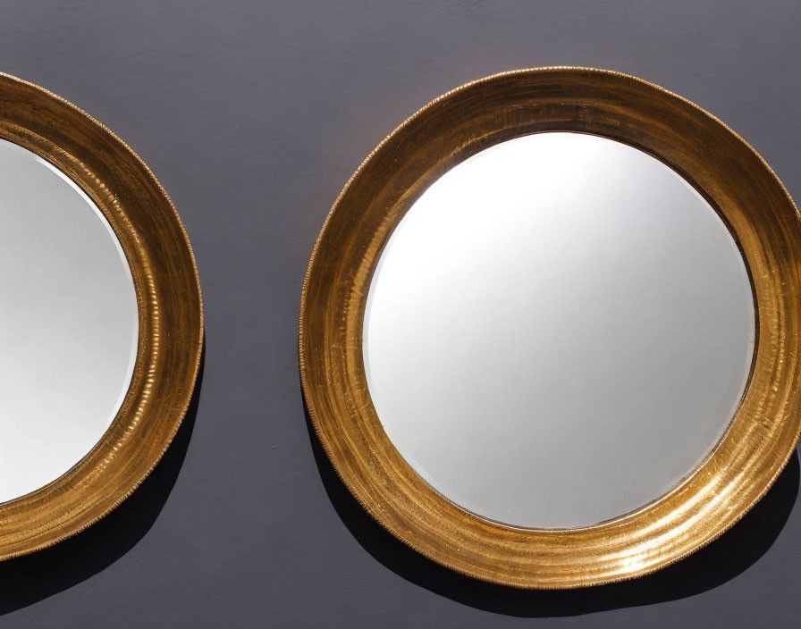 Golden framed mirrors on gray wall with soft shadows, one partially cropped.