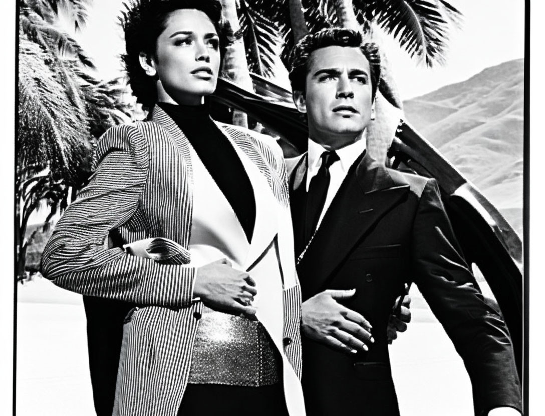 Monochrome image: Man in suit, woman in glittery outfit, posing with palm trees