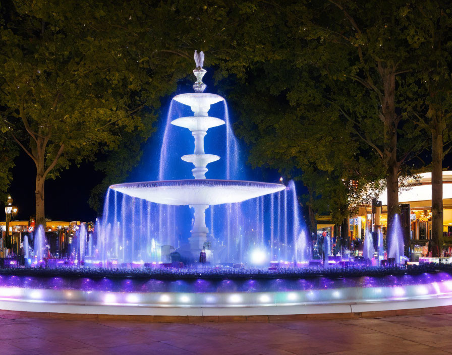 Nighttime multi-tiered fountain with blue lights and trees in dark sky