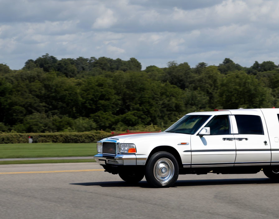 White Limousine Driving on Road with Cloudy Sky & Greenery