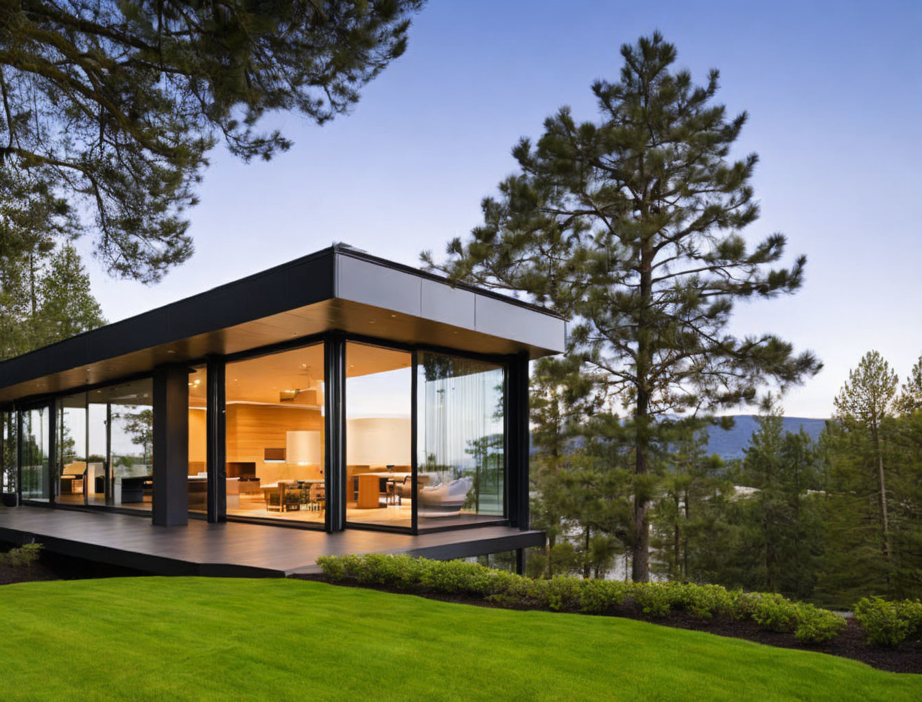 Glass-walled house with flat roof in pine tree setting at dusk