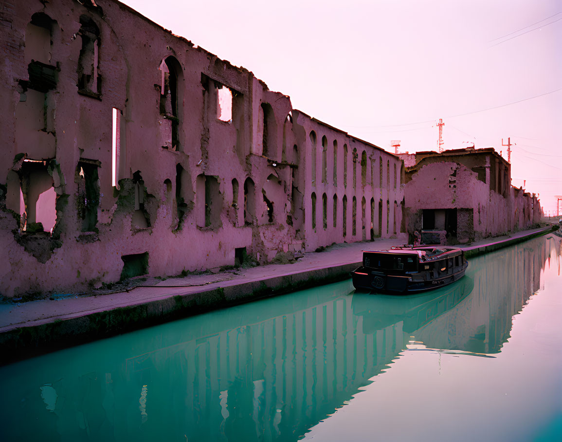 Abandoned building near canal with boat under pink dusk sky