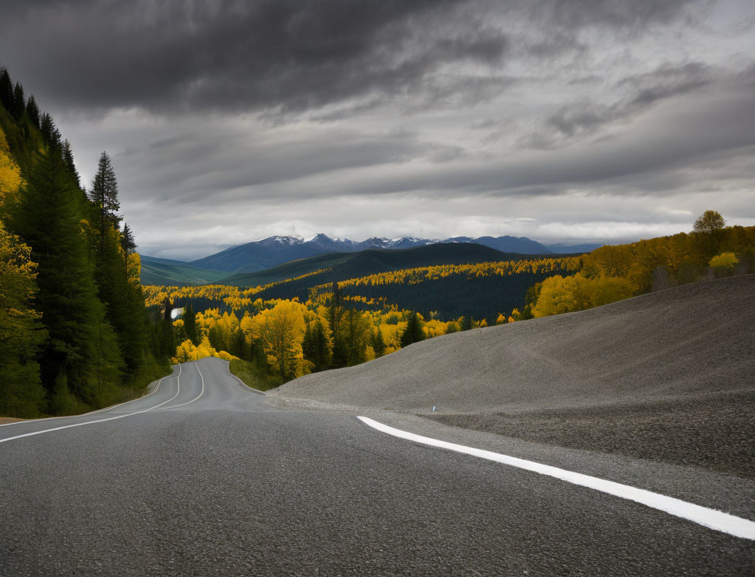 Scenic mountain road with autumn trees under dark skies