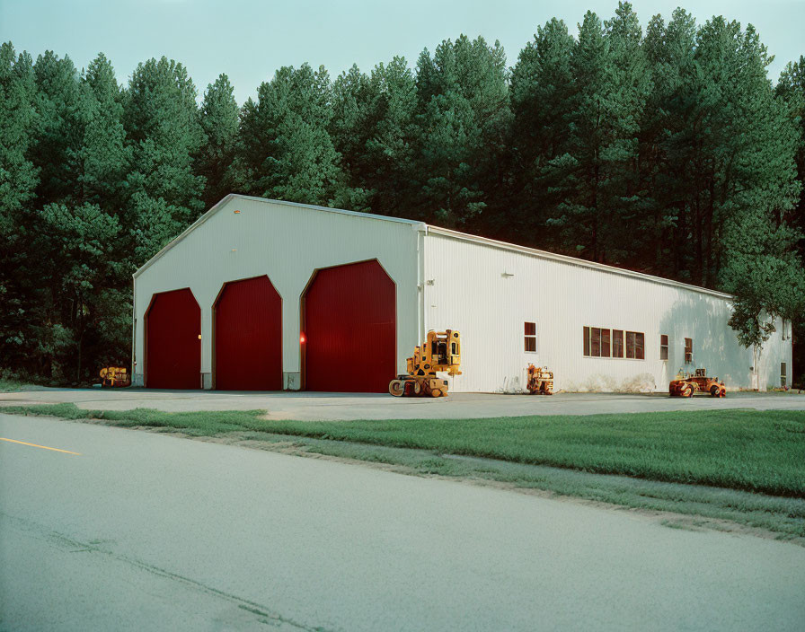 White Industrial Building with Red Doors and Construction Machinery by Road