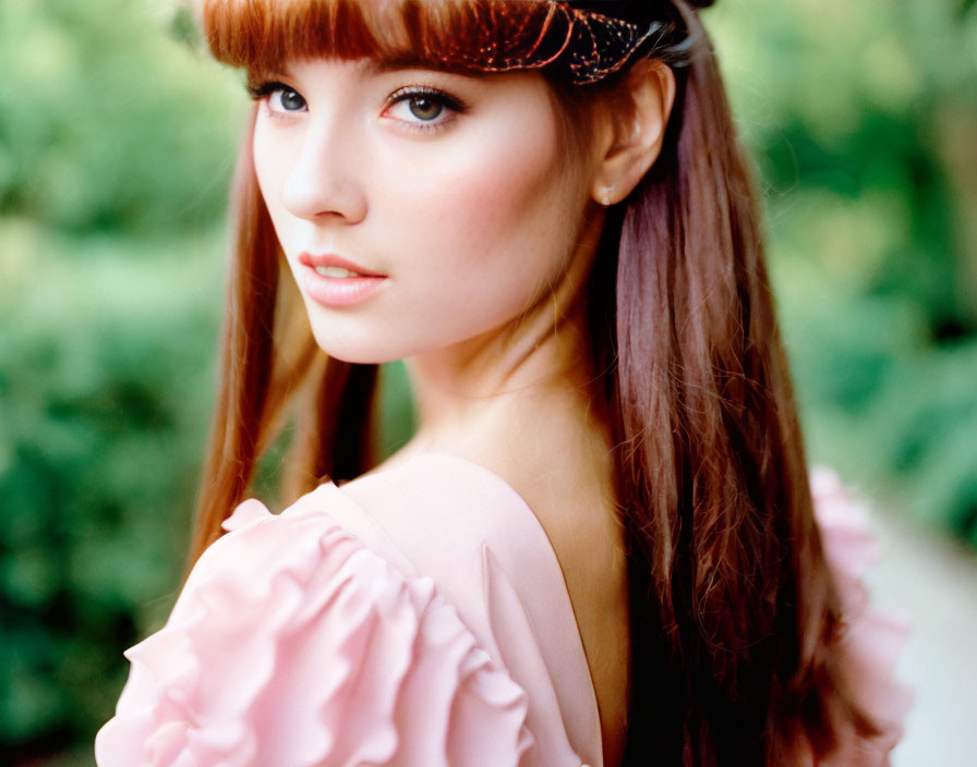 Young woman portrait with brown hair, pink ruffled top, and green background