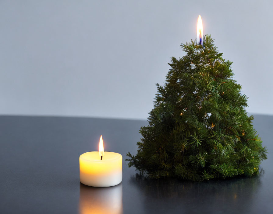 Burning candle next to flaming Christmas tree on table