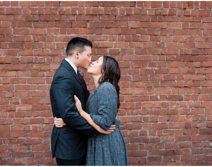 Formal couple kissing in front of brick wall