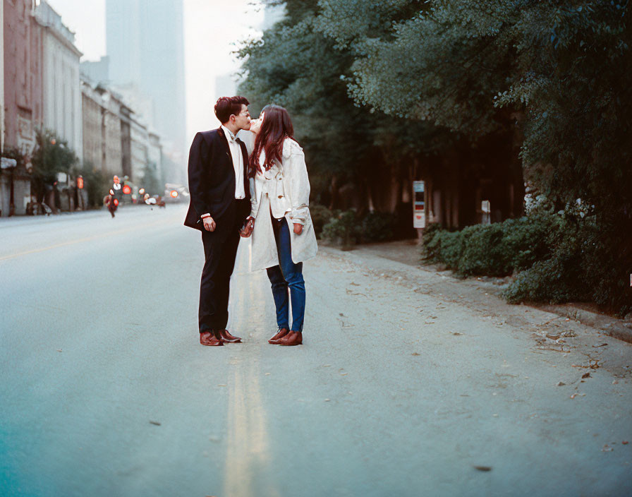 Couple kissing in deserted city street with trees and soft evening light