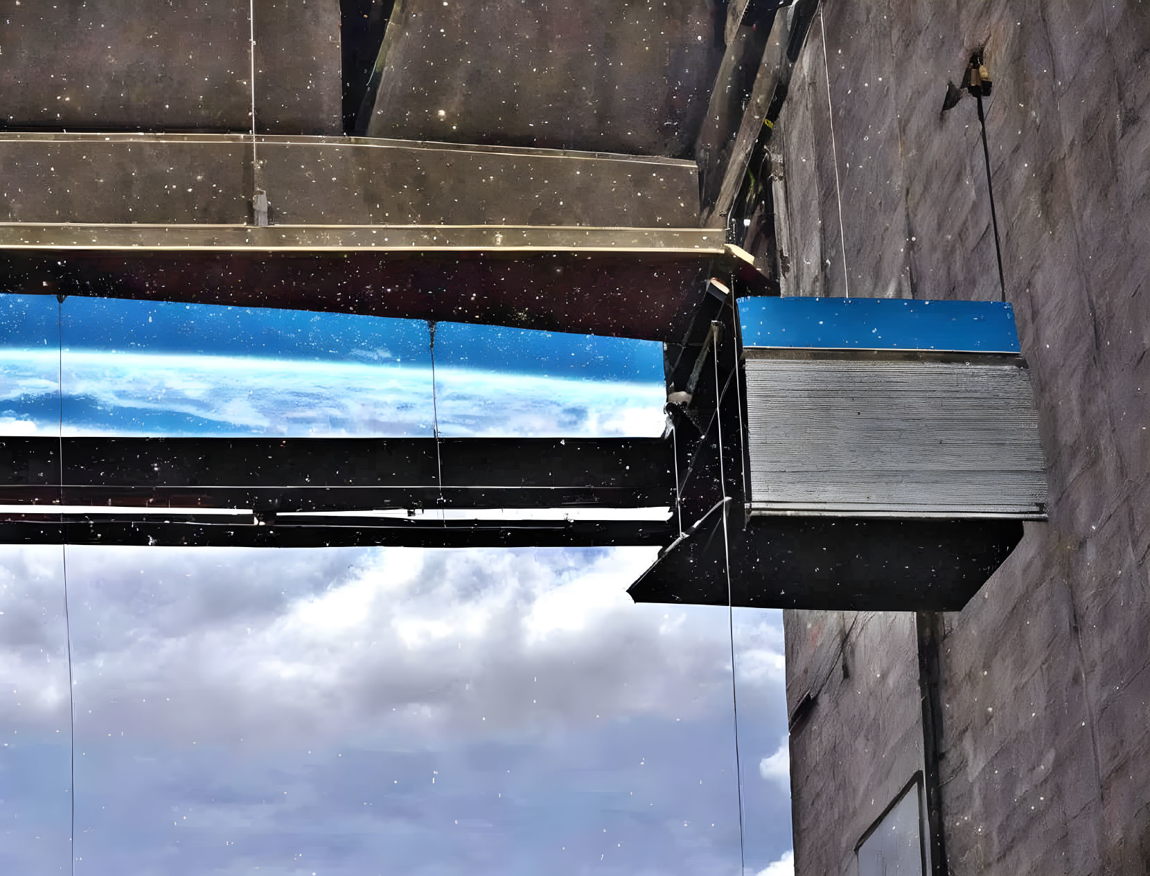 Glass-bottom building overlooking blue sky with clouds and dark structure with cables