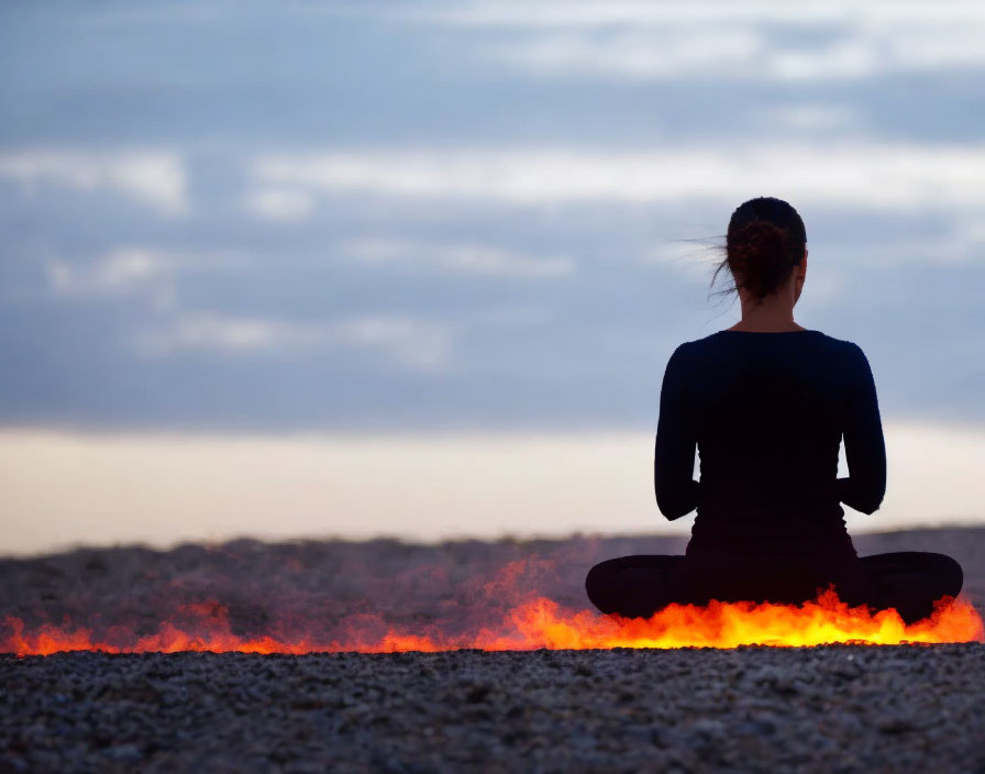 Person meditating in silhouette with glowing orange light on dusky sky