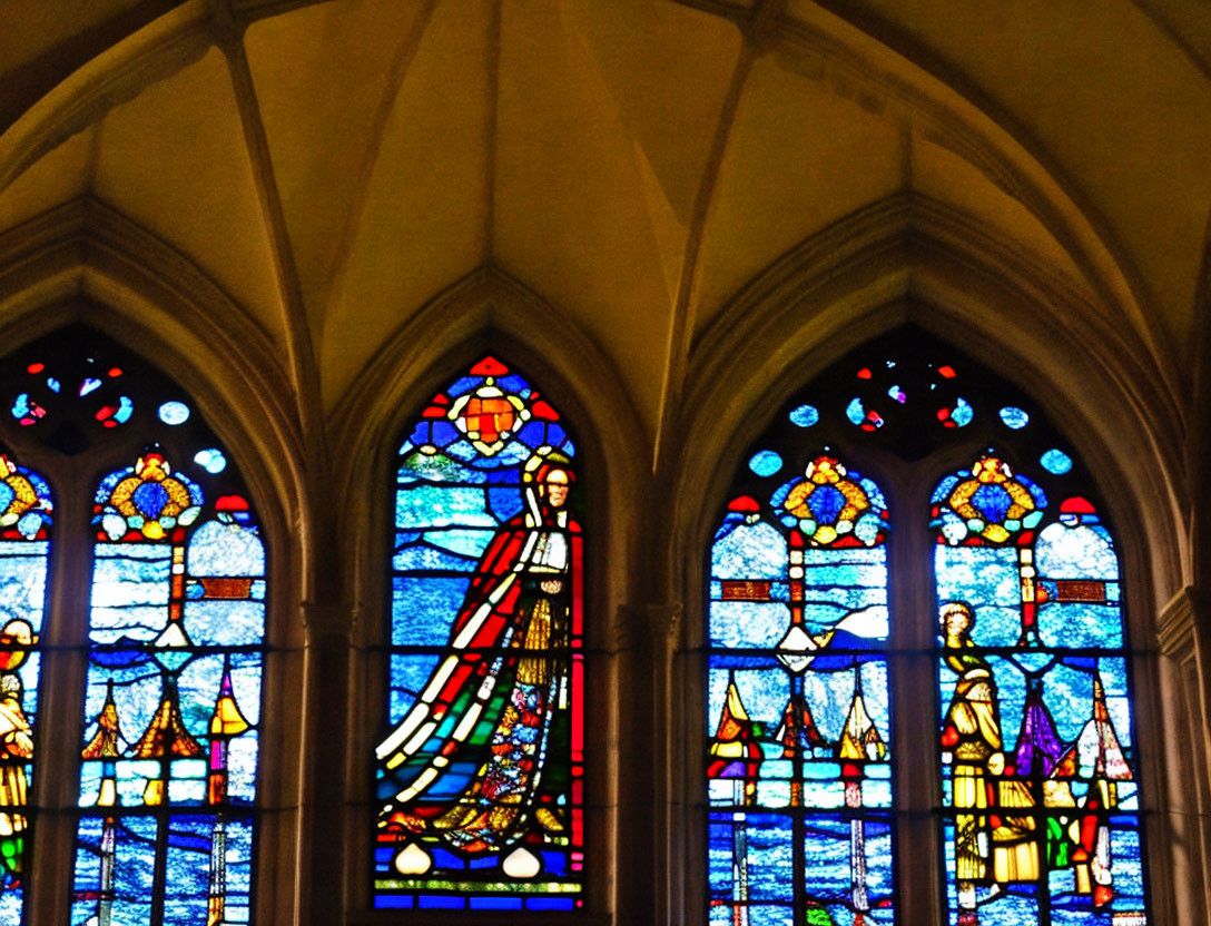 Colorful Gothic-style stained glass windows with religious figures and motifs in arch setting.