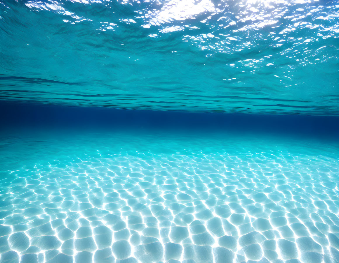 Sun rays shining through crystal-clear blue water illuminating sandy ocean floor.