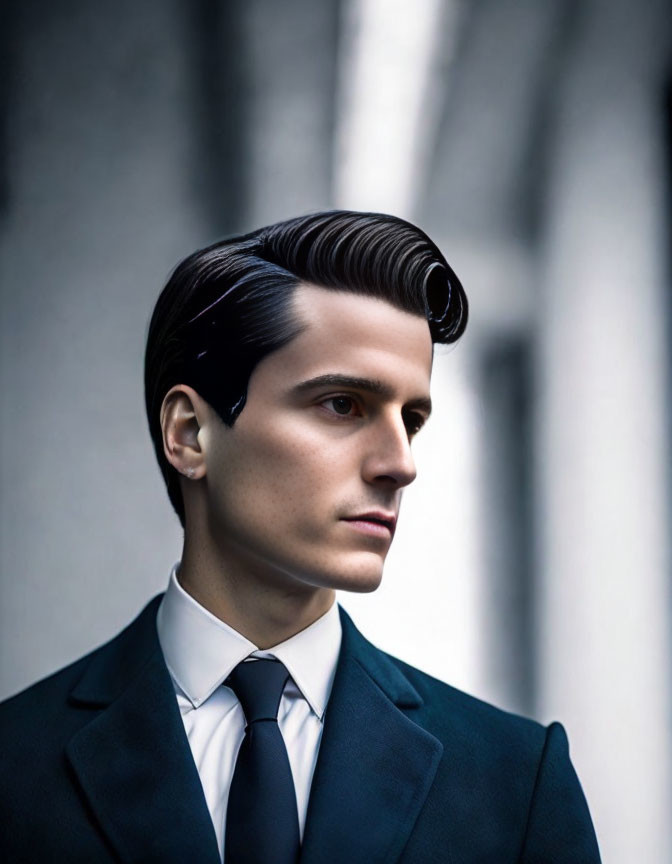 Man in Dark Suit with Slicked-Back Hair Poses Against Architectural Background