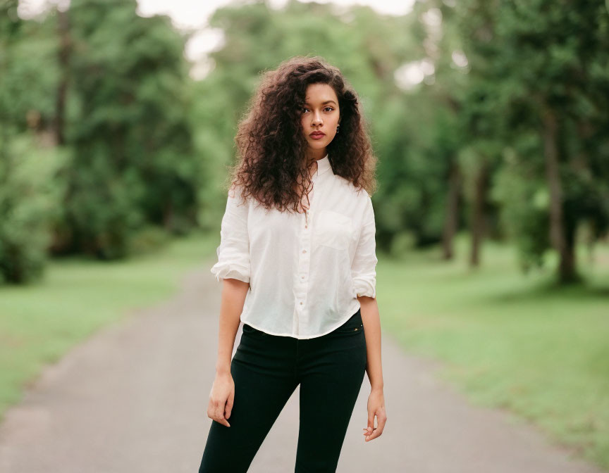 Curly-haired woman in white shirt and black pants on path with greenery