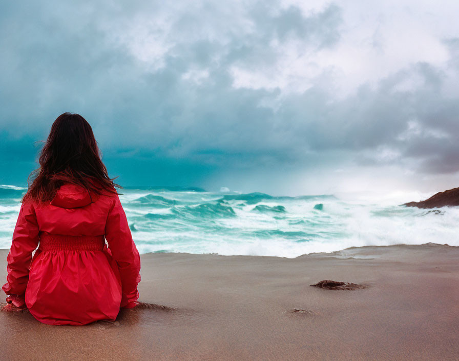 Person in Red Jacket Sitting on Beach During Stormy Weather