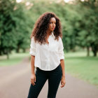 Curly-haired woman in white shirt and black pants on path with greenery