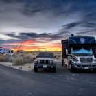 Desert camping scene at dusk with tent, RV, classic car, and accessories