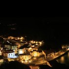 Panoramic Mediterranean village night scene with starry skies, glowing buildings, lighthouse, and moon