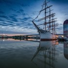 Sailing ship with billowing sails near rock formation at sea at sunset