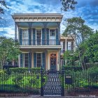 Vintage two-story house with iron balconies in lush greenery under clear blue sky.