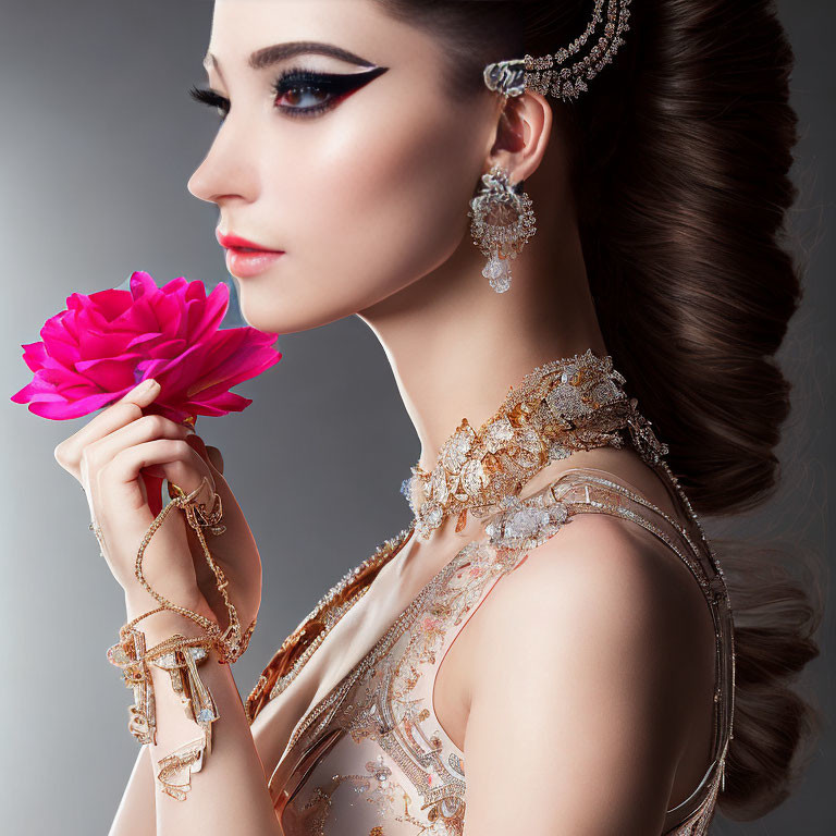 Elegant woman with elaborate jewelry holding a vibrant pink flower