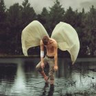 Melancholic angel with bloodstained wings in misty forest scene